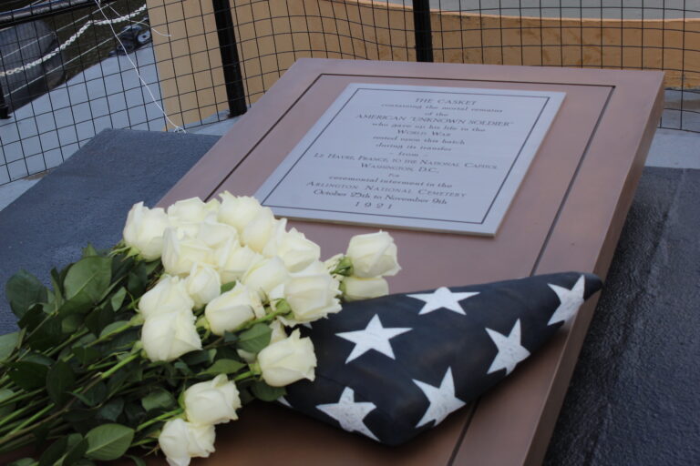 The historical marker with an American flag and white roses placed on top of it for the Unknown Soldier of WWI on Cruiser Olympia